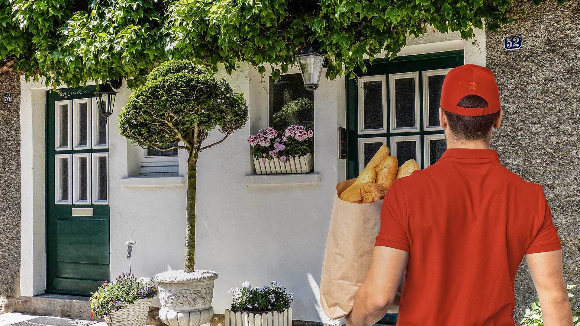 Lieferant (von hinten zu sehen) steht mit Brottüte vor einer Haustür.