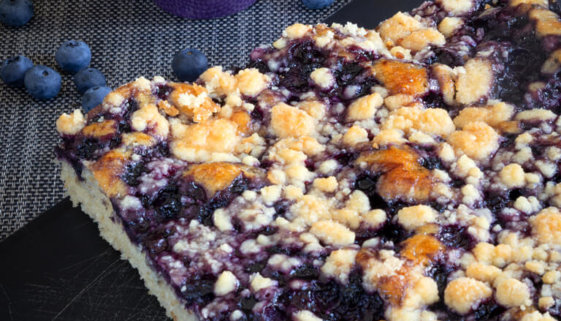 Dinkel-Heidelbeer-Kuchen auf Brett und Heidelbeeren in Schale